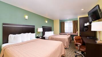 A hotel room with two beds, a desk with a computer, a TV, and a window with curtains.