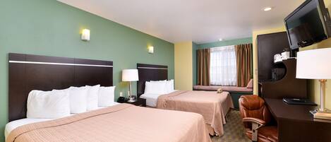 A hotel room with two beds, a desk with a computer, a TV, and a window with curtains.