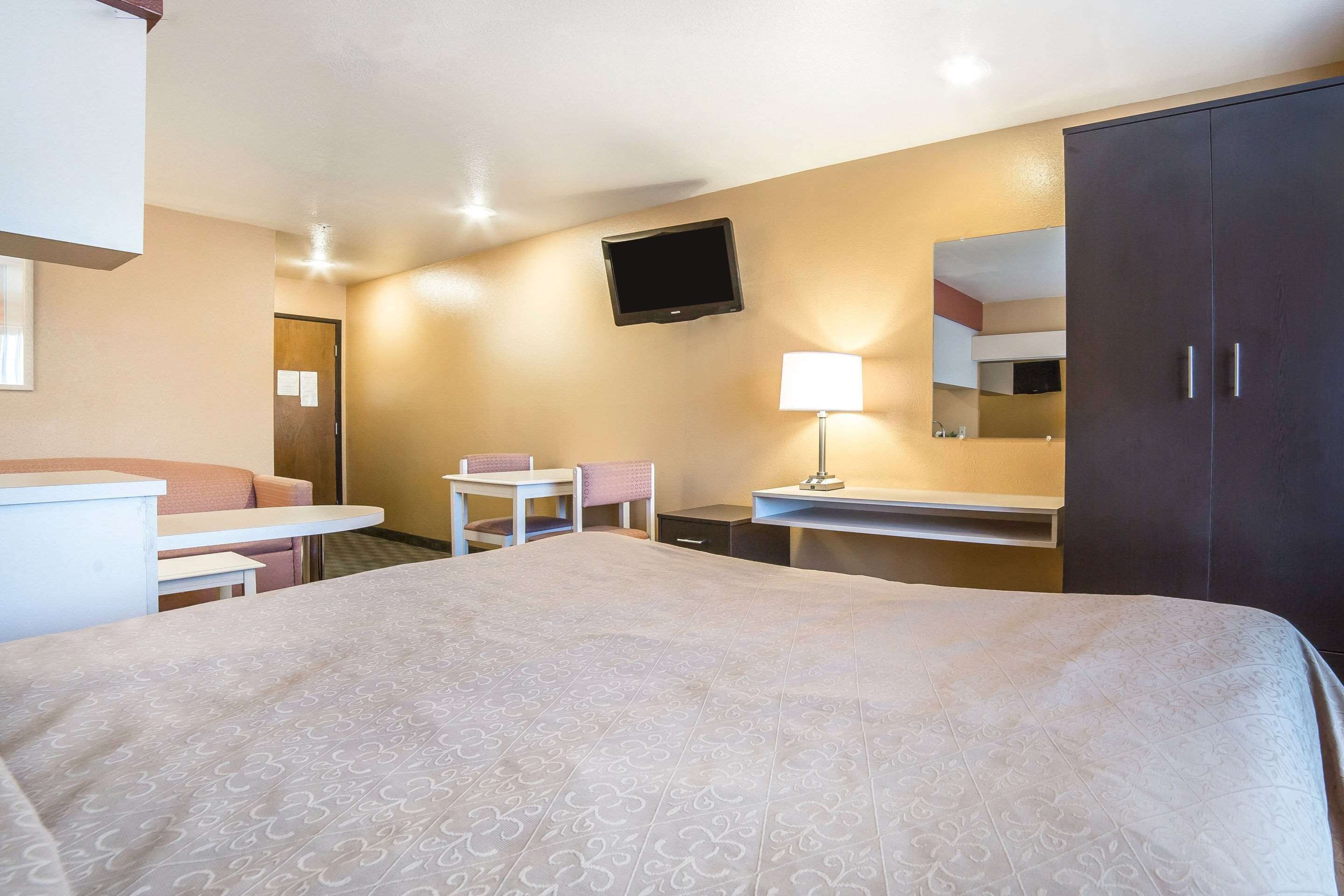 A hotel room with a bed, a desk, a chair, a TV, a lamp, and a wardrobe.