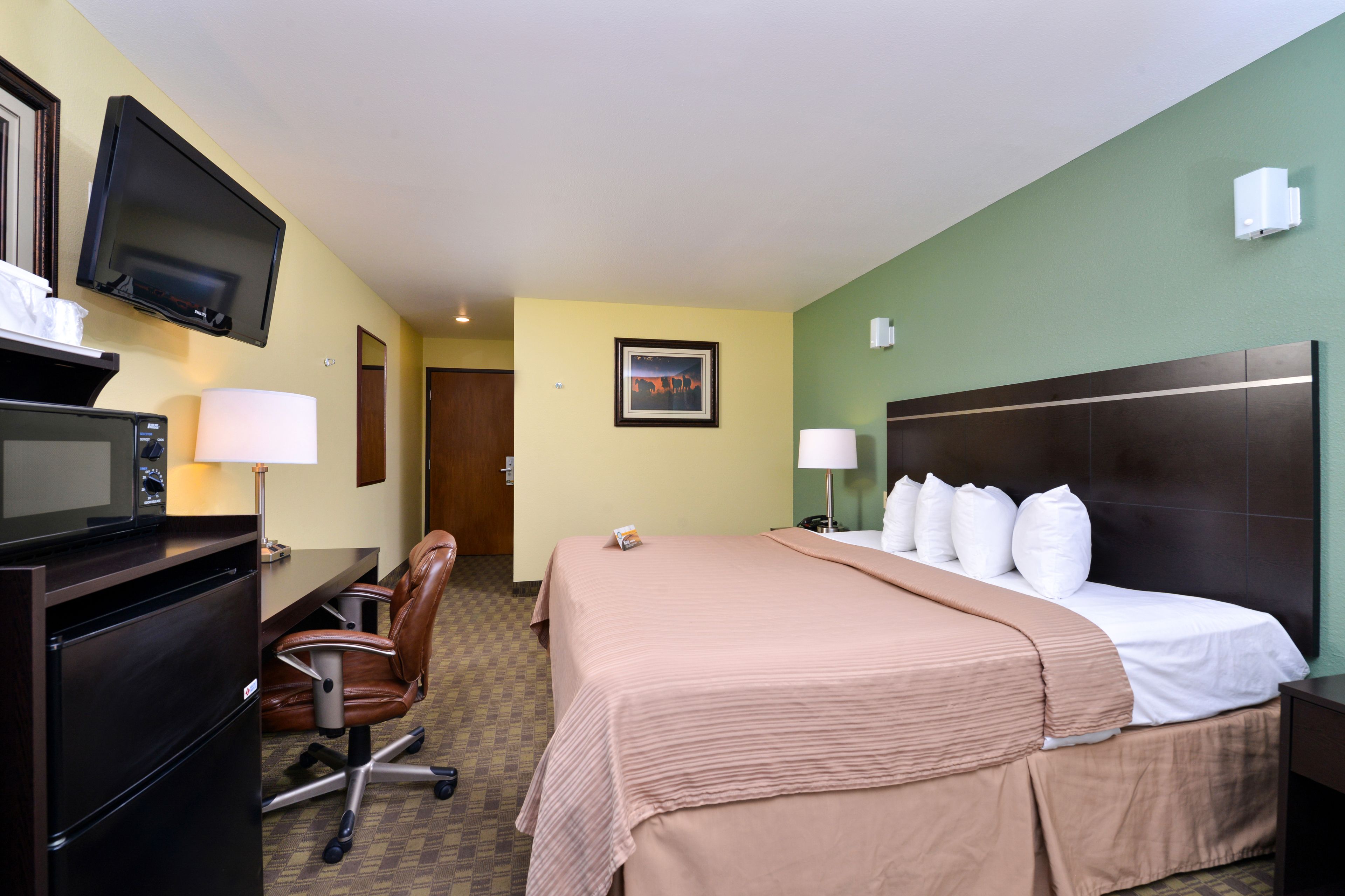 A hotel room with a bed, desk, chair, television, and a framed picture on the wall.