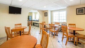 A dining area with multiple wooden tables and chairs, a television mounted on the wall, and a kitchen area in the background. - Quality Inn & Suites Elko (Elko)