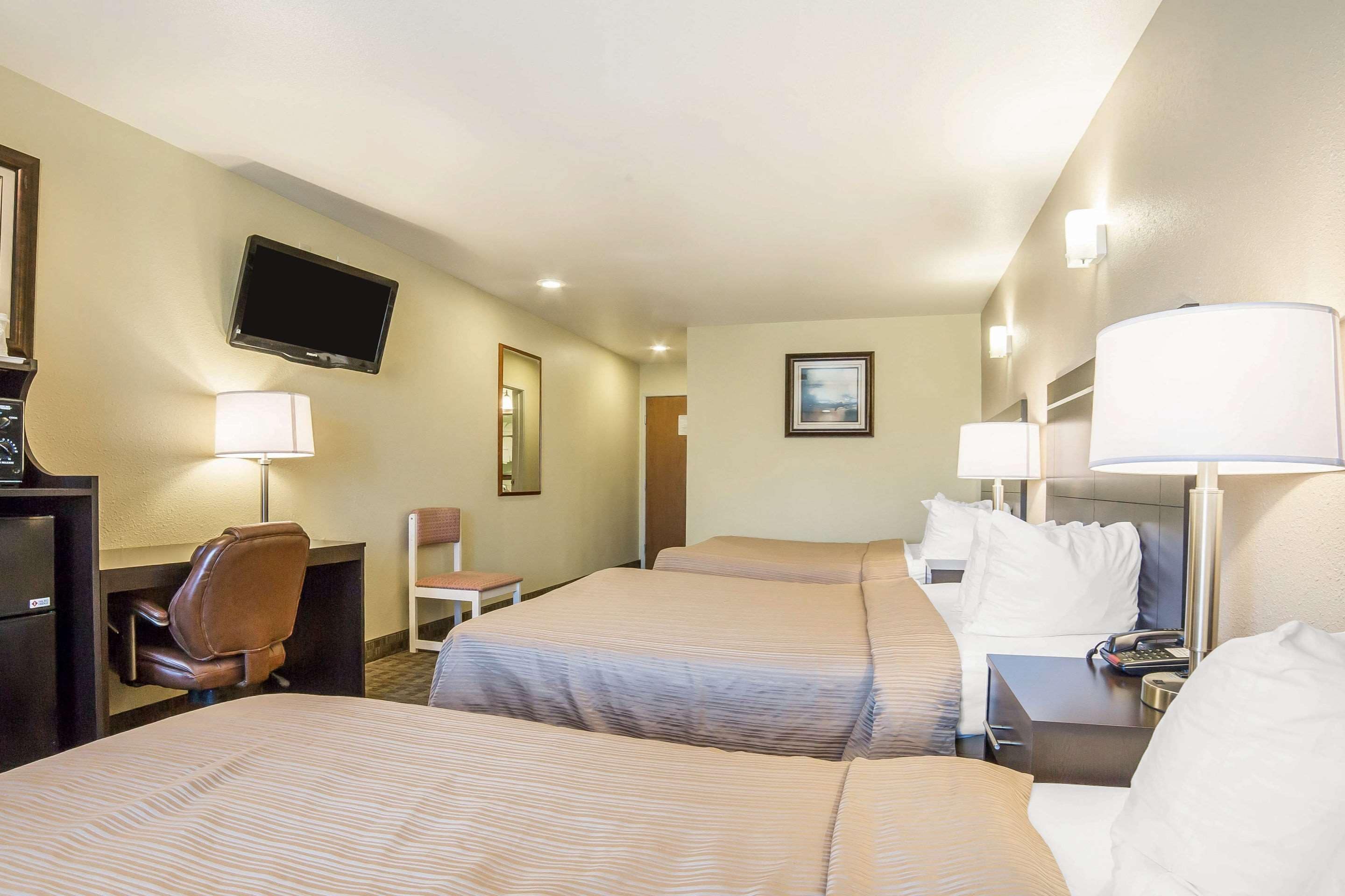 A hotel room with two beds, a desk, a chair, a TV, and a lamp.