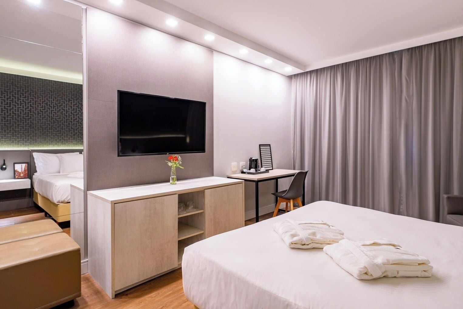 A modern hotel room with a large bed, a desk, a flat-screen TV, and a window with curtains.