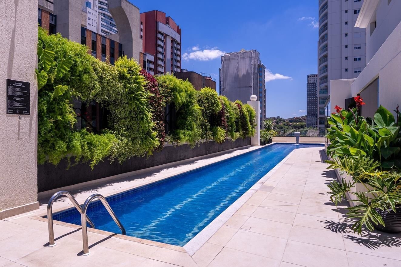 Ein Schwimmbecken mit einer Metallleiter, umgeben von einer gefliesten Terrasse und üppigem Grün.