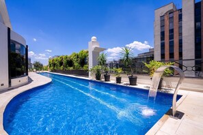 Una piscina de disseny modern, envoltada d'edificis i vegetació.