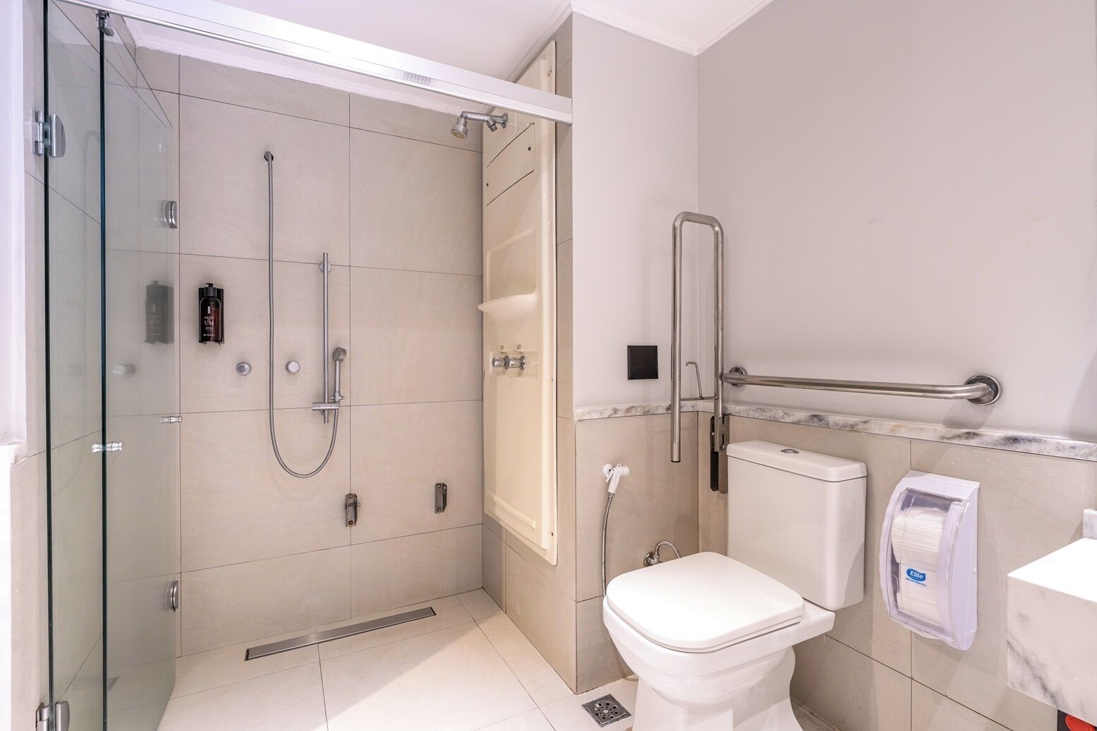 A modern bathroom with a glass-enclosed shower, a toilet, and a hand dryer.