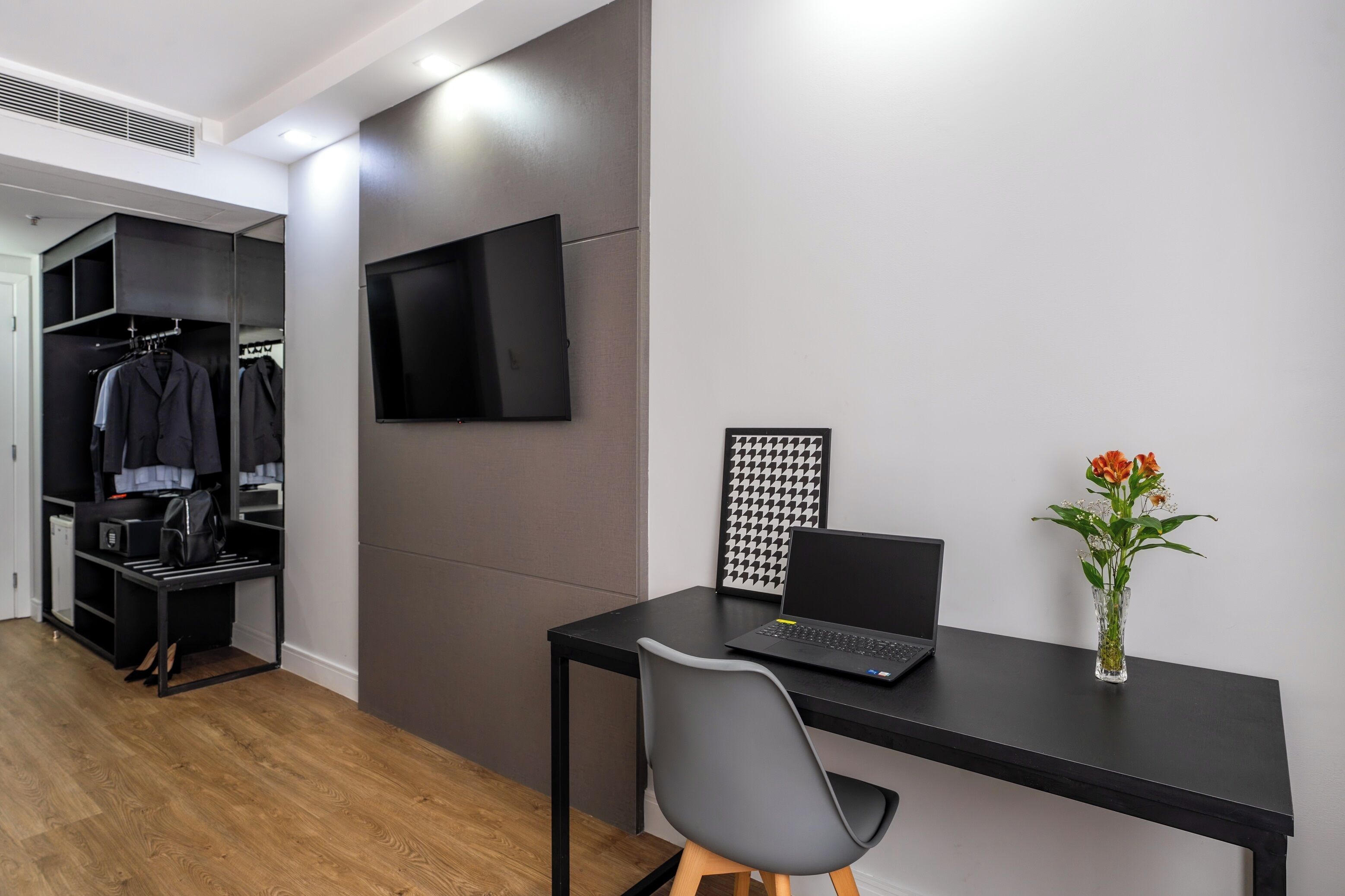 A modern room with a desk, chair, laptop, TV, and a closet with hanging clothes.