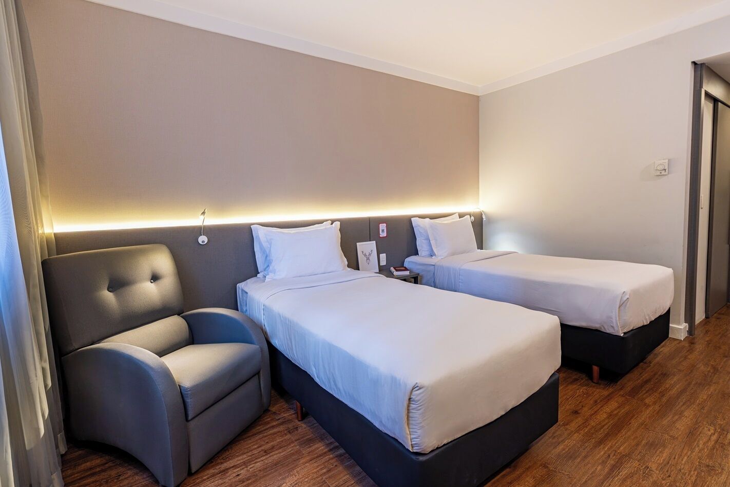 Een hotelkamer met twee bedden, een stoel en een houten vloer.