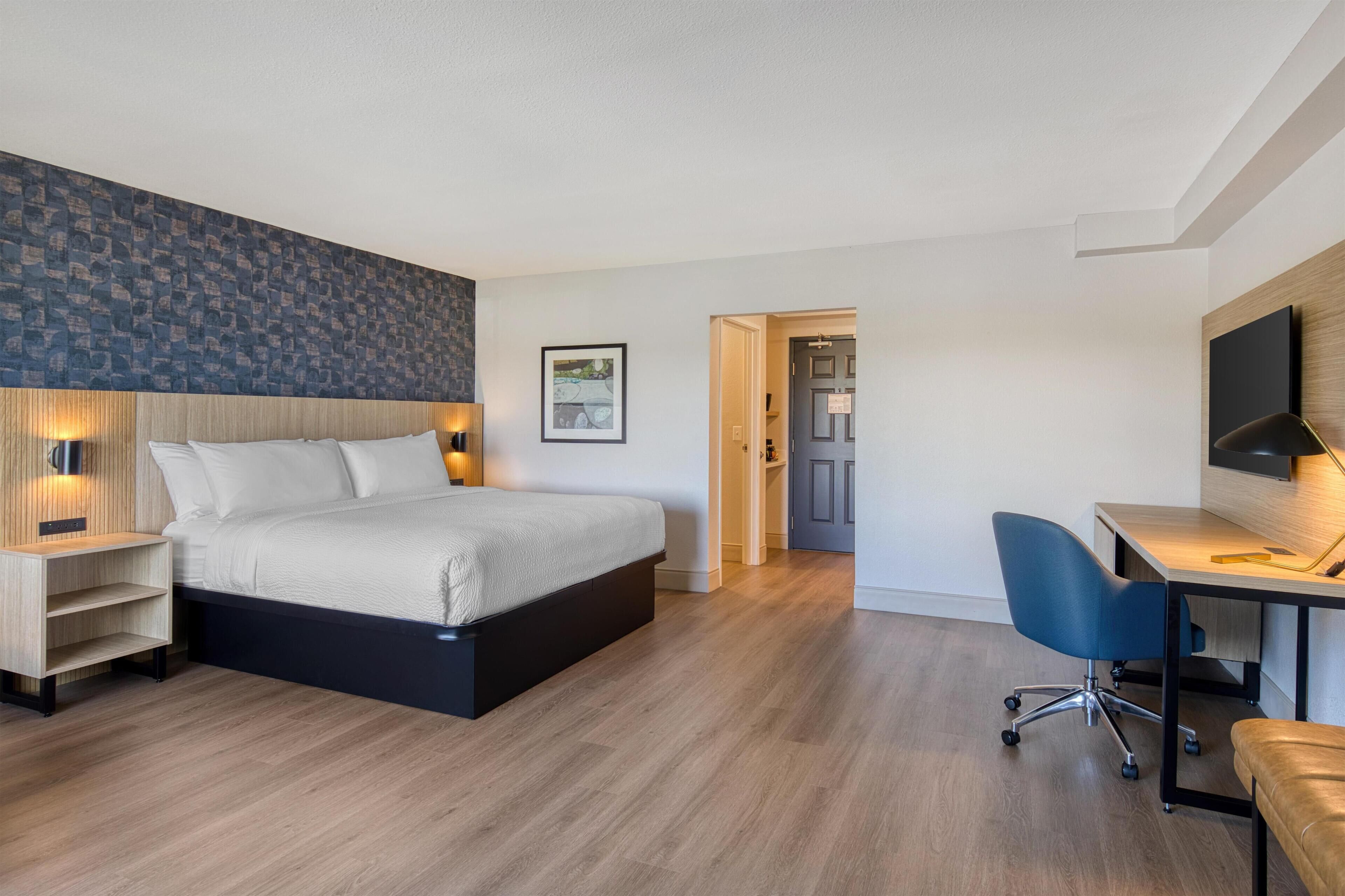Una habitación de hotel moderna con cama, escritorio, silla y un pequeño rincón de descanso.