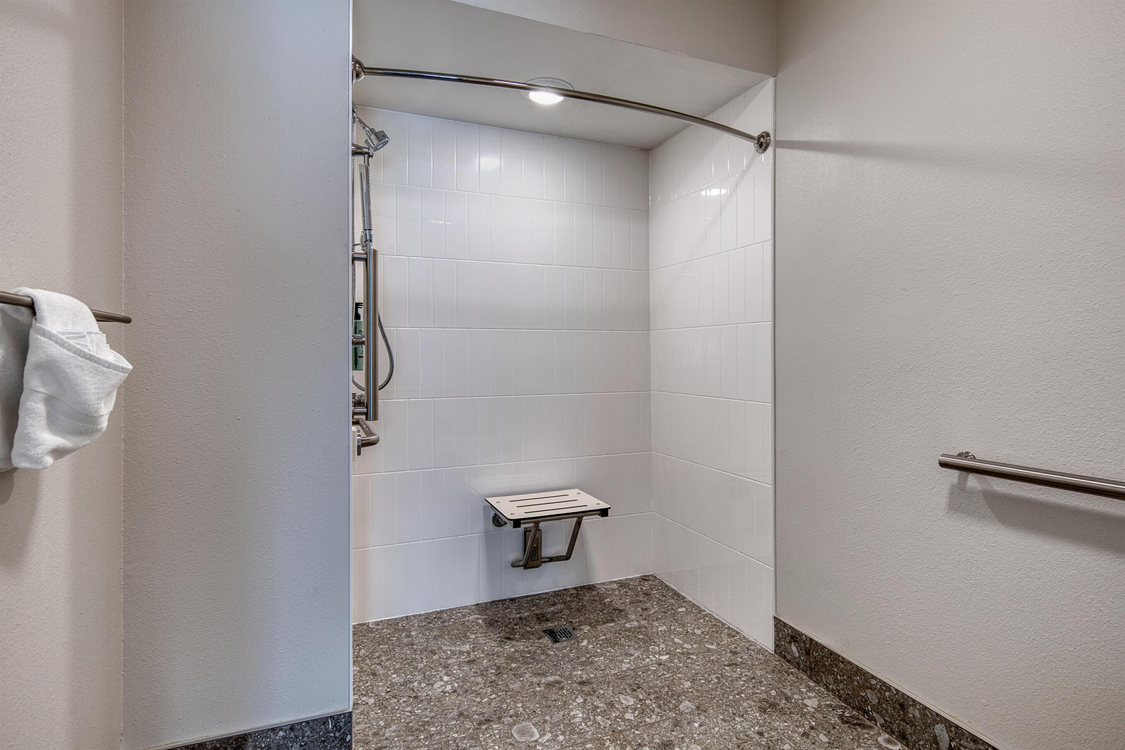 A shower area with white tiled walls, a granite floor, and a grab bar on the right wall.