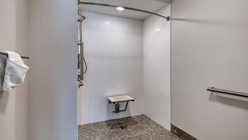 A shower area with white tiled walls, a granite floor, and a grab bar on the right wall.