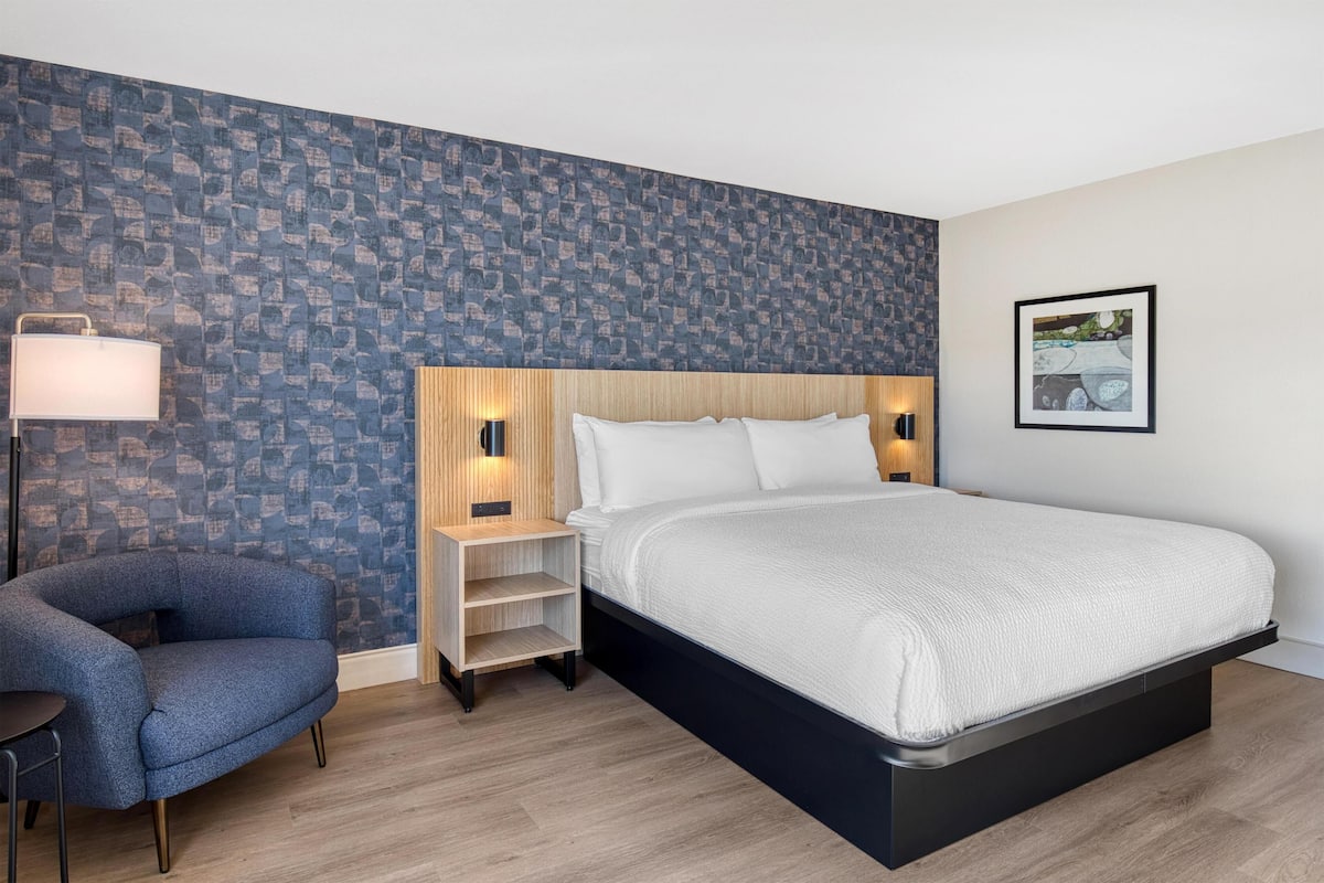 Ein modernes Hotelzimmer mit einem großen Bett, einem Sessel, einem Nachttisch und einer Wand mit strukturiertem Wandpapier.