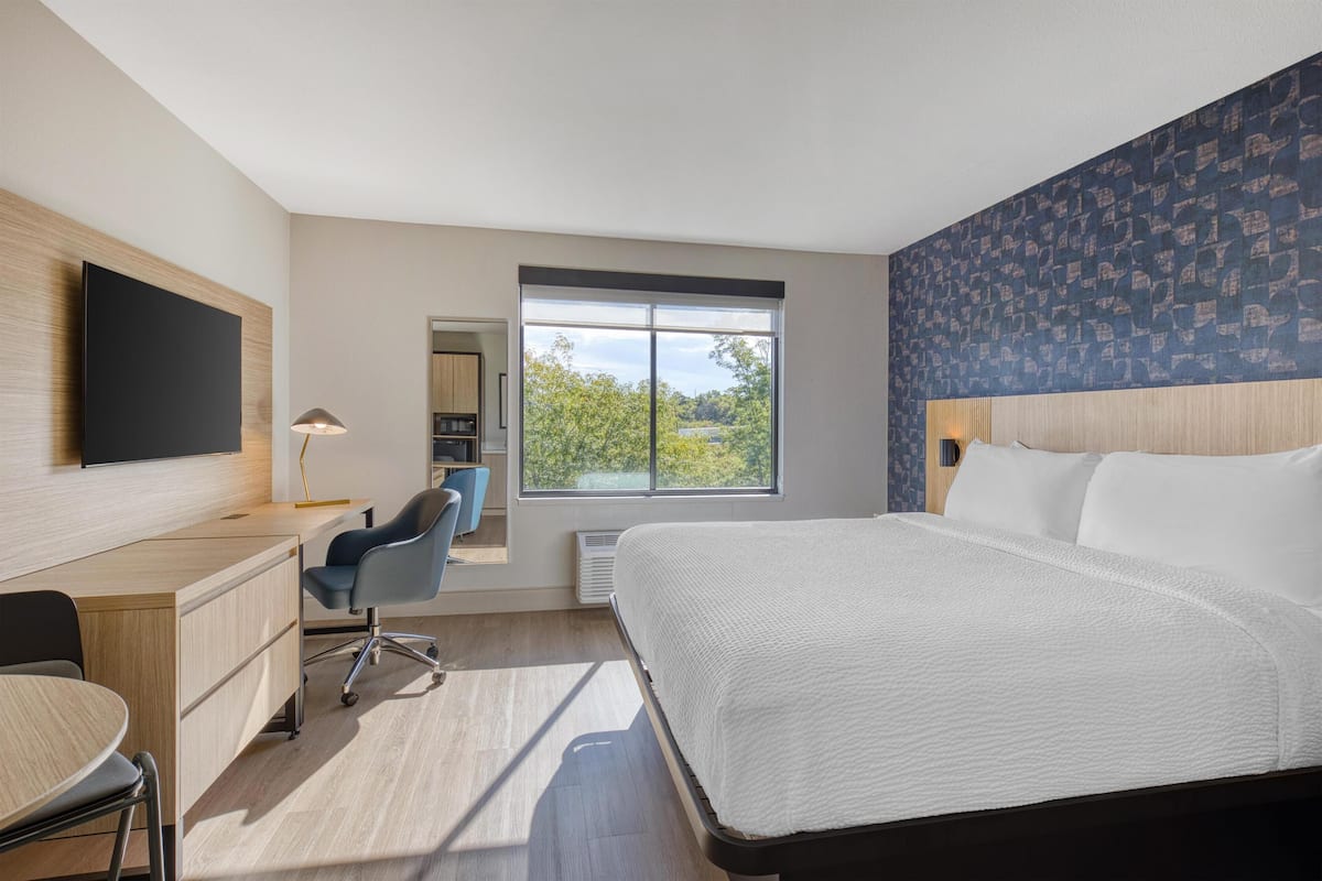 Ein modernes Hotelzimmer mit einem großen Bett, einem Schreibtisch, einem Sessel und einem Fernseher.