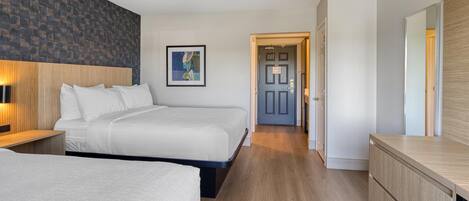 Habitación de hotel con dos camas, un cabecero de madera, una mesita de noche con lámpara, un aparador y un cuadro enmarcado en la pared.