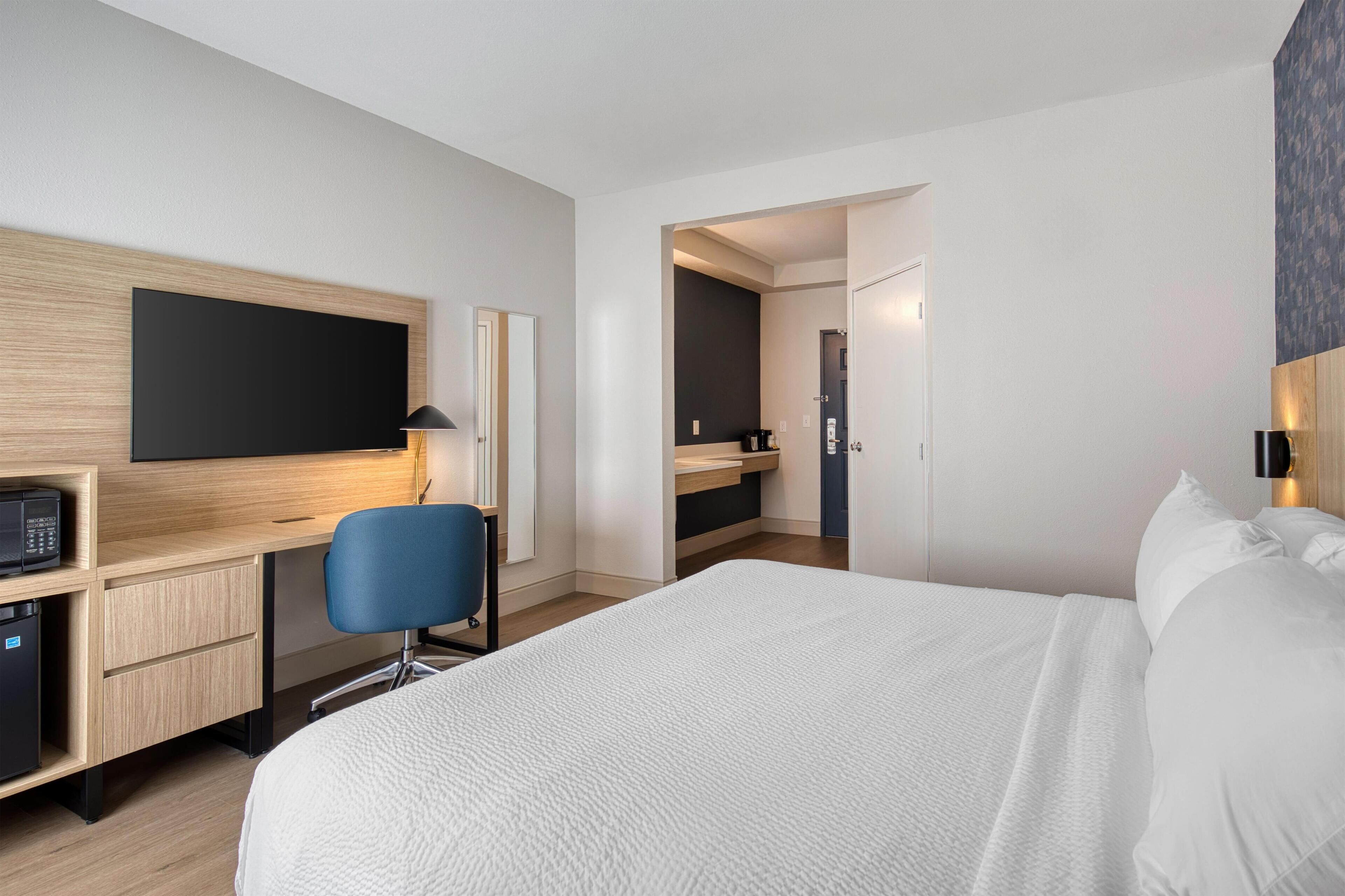 Una habitación de hotel moderna con una cama grande, un escritorio con computadora, una silla y un televisor de pantalla plana.