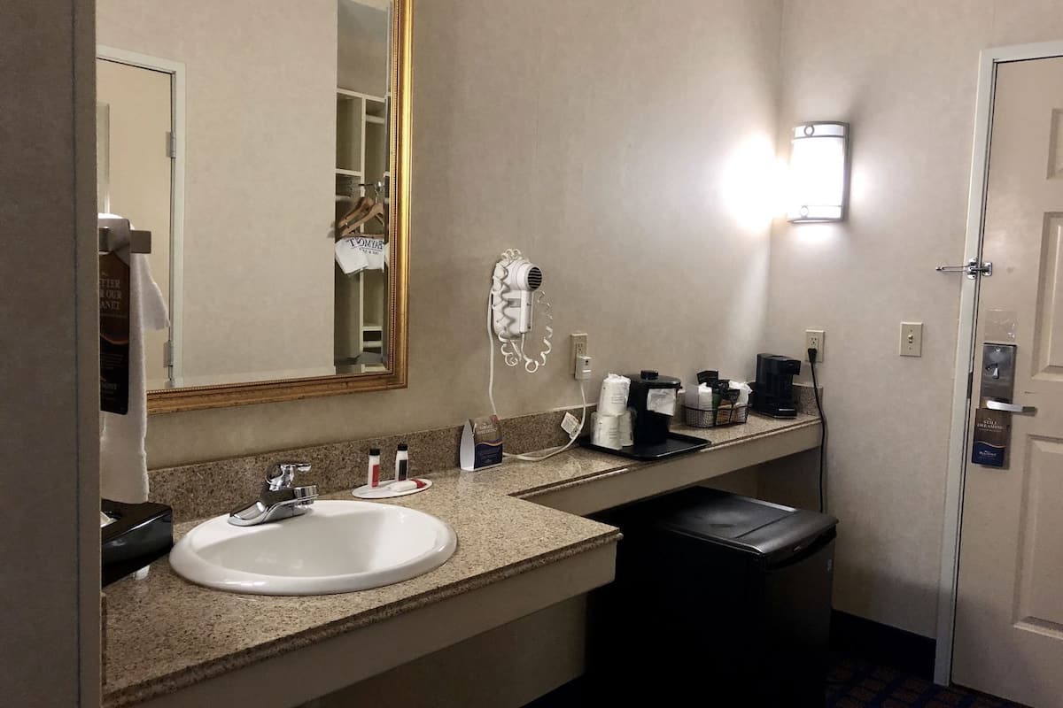 Ein Hotelbad mit Waschbecken, Spiegel, Fön und Pflegeprodukten.