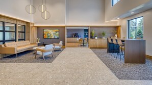 A spacious lobby with a modern design, featuring a seating area with a sofa and chairs, a small coffee table, and a bar area with stools. - Best Western Byron Center (Byron Center)