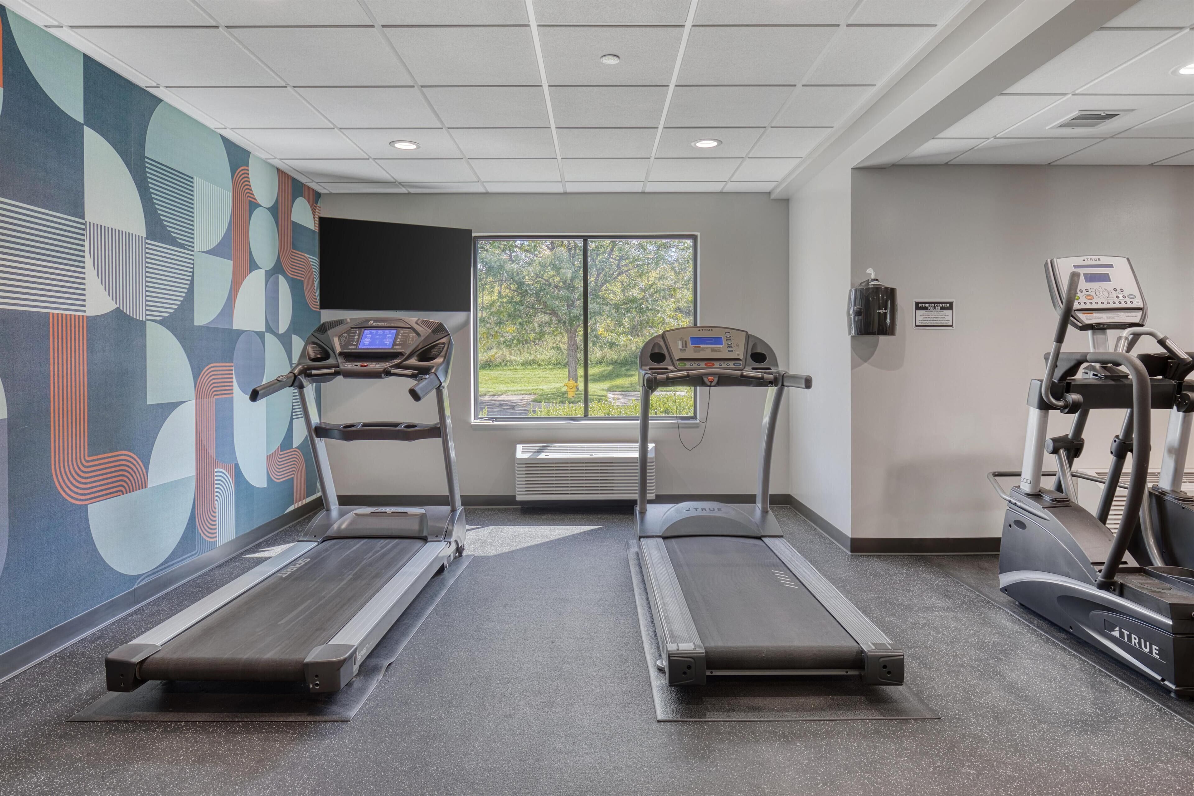 A gym with two treadmills, a stationary bike, and a large window with a view of trees.