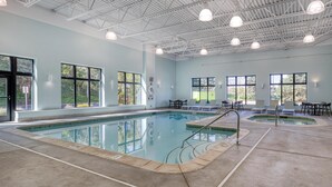 An indoor swimming pool with clear glass walls, a high ceiling with metal beams, and multiple windows. - Best Western Byron Center (Byron Center)