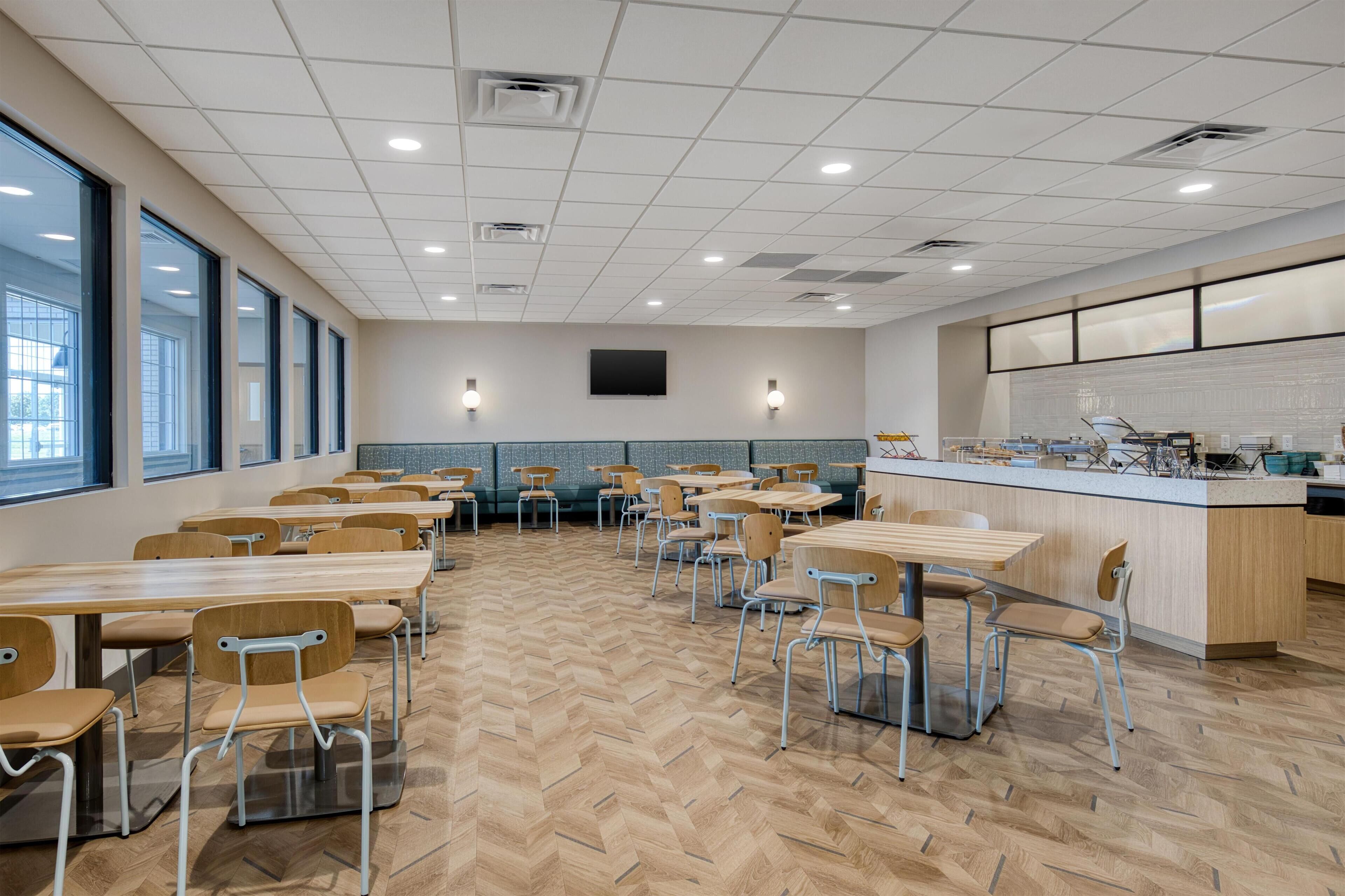 A modern dining area with wooden tables and chairs, a counter with a menu, and a large window on one side.