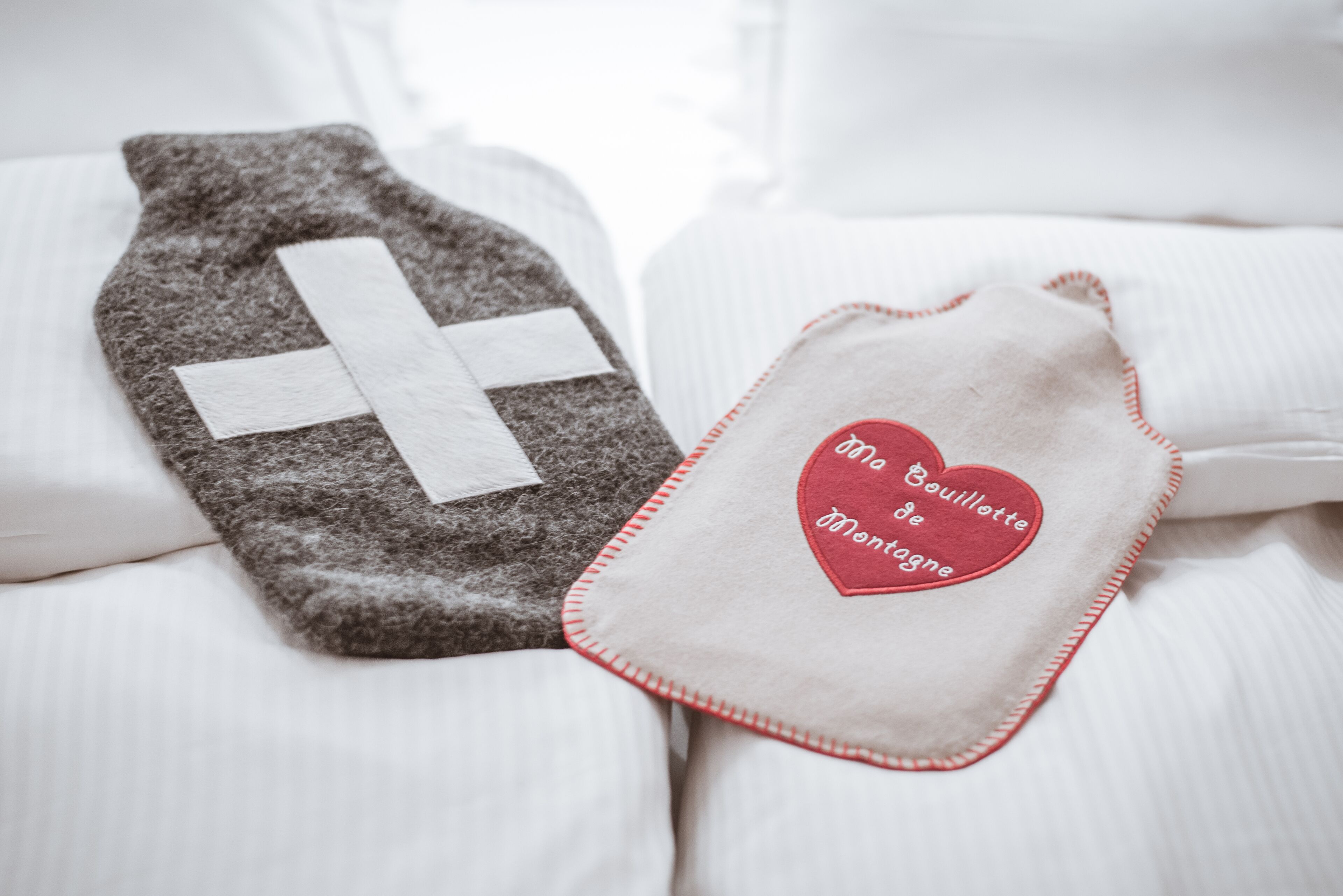 A bed with a gray blanket and a white pillow with a red heart-shaped pillowcase.