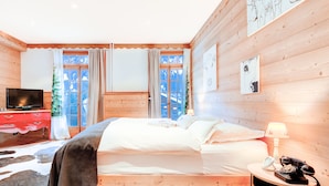 Une chambre à coucher aux murs lambrissés, avec un lit, un téléviseur, une commode rouge et des œuvres d’art accrochées aux murs.