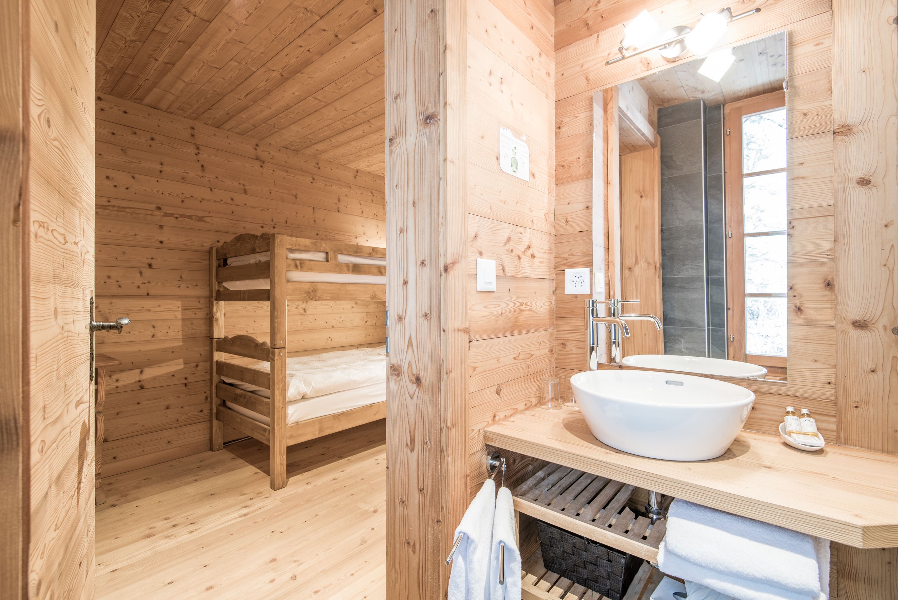 Interior de una cabaña de madera con una litera, un lavamanos grande y un espejo.