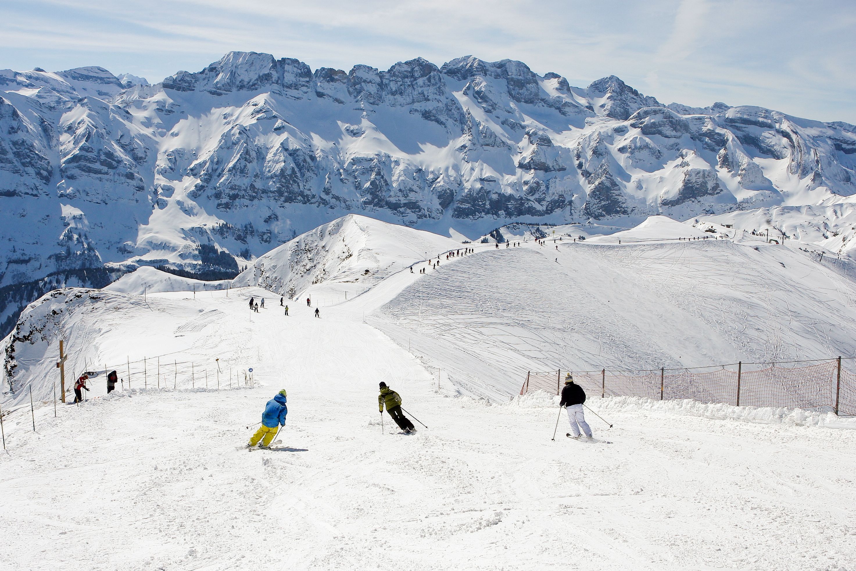 A snowy ski slope with skiers and a mountainous backdrop.