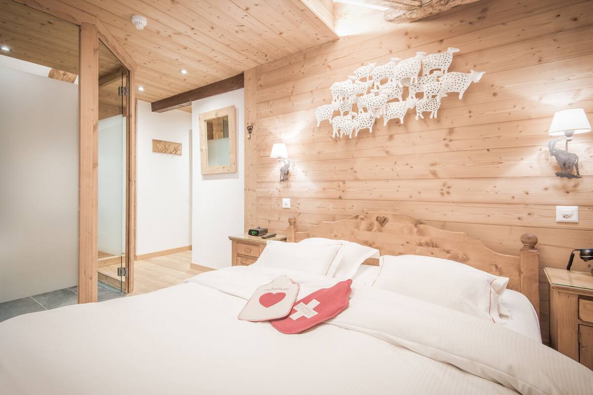 Ein Schlafzimmer mit Holzboden, einem Bett mit weißen Leinen, einem Nachttisch mit Lampe und einer Wand mit Schaf-Motiven.