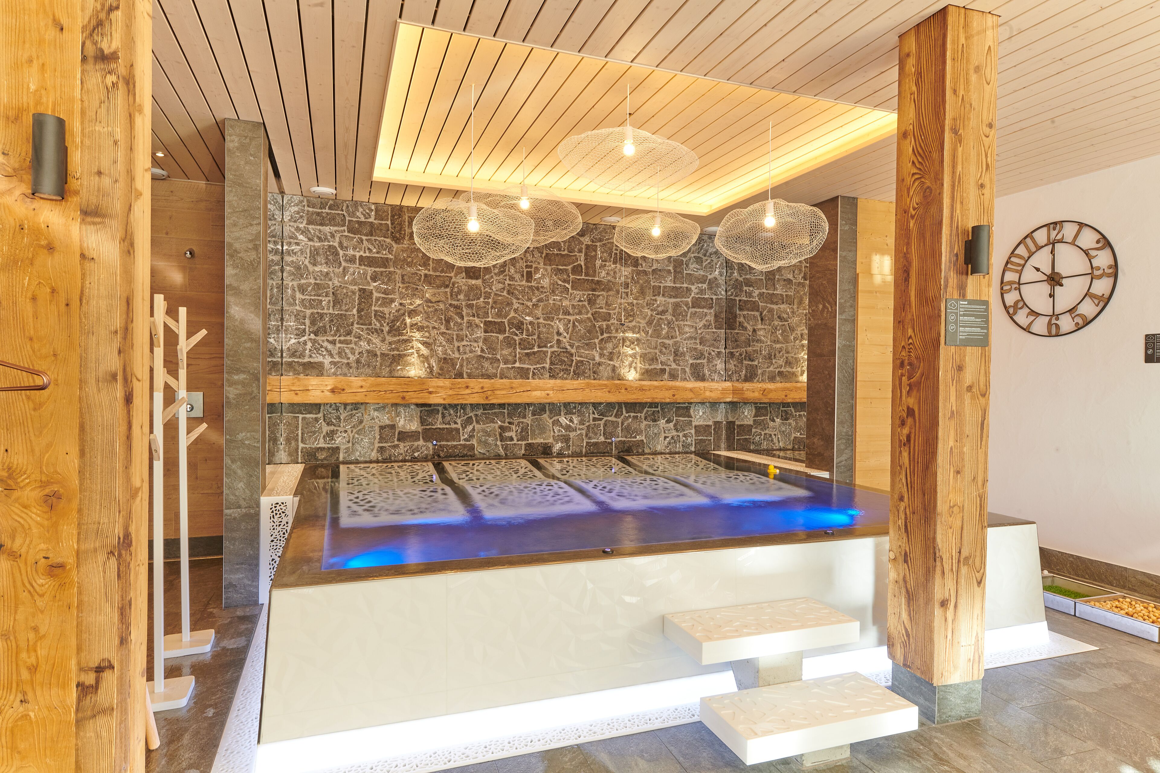 Een moderne spa met een stenen muur, houten balken en een verwarmde vloer.