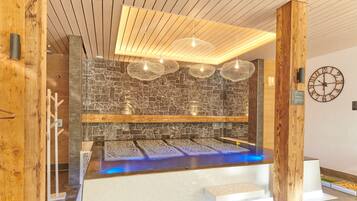 Een moderne spa met een stenen muur, houten balken en een verwarmde vloer.