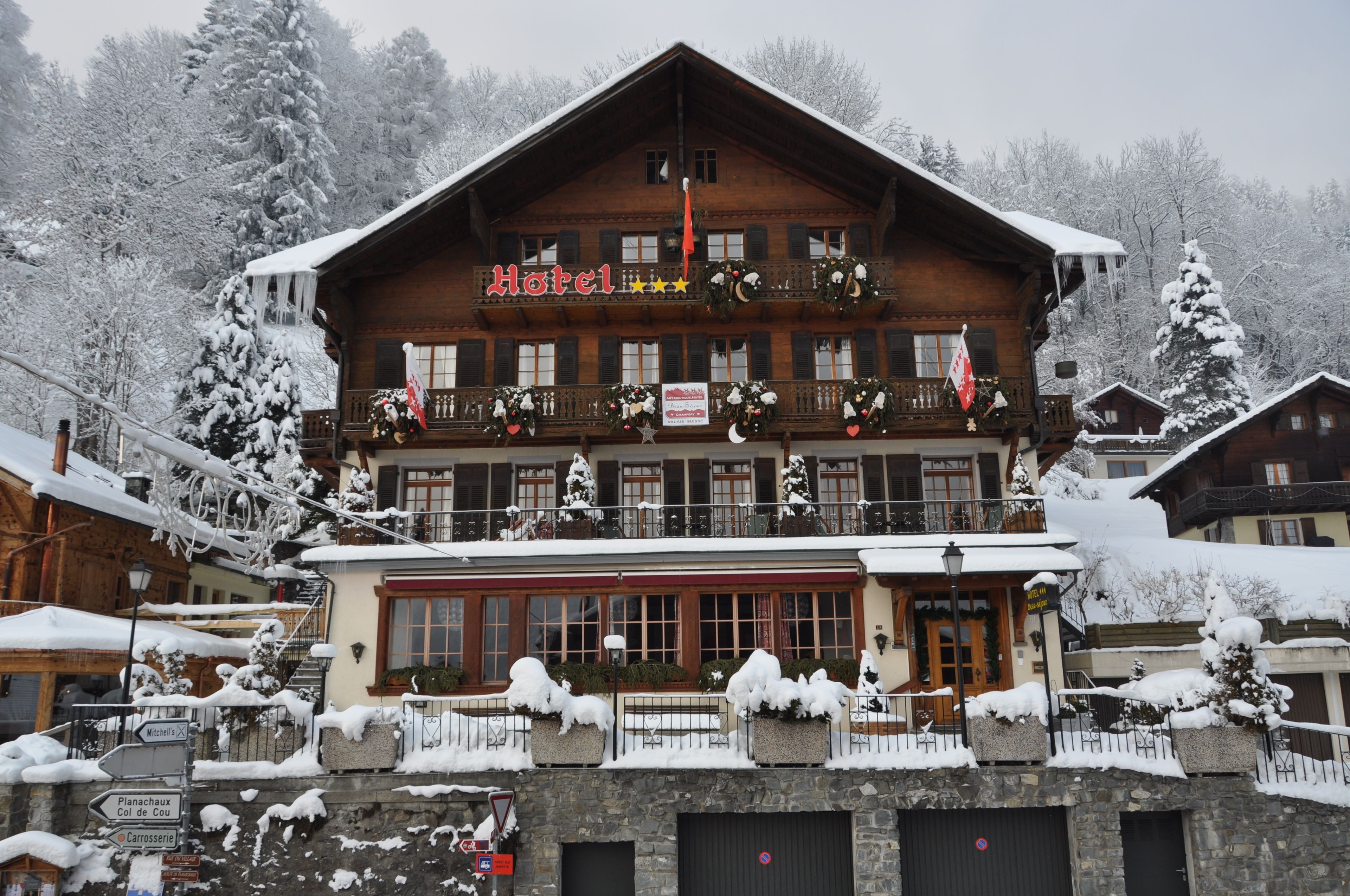 A wooden hotel with balconies decorated with wreaths and flags, surrounded by snow-covered trees.