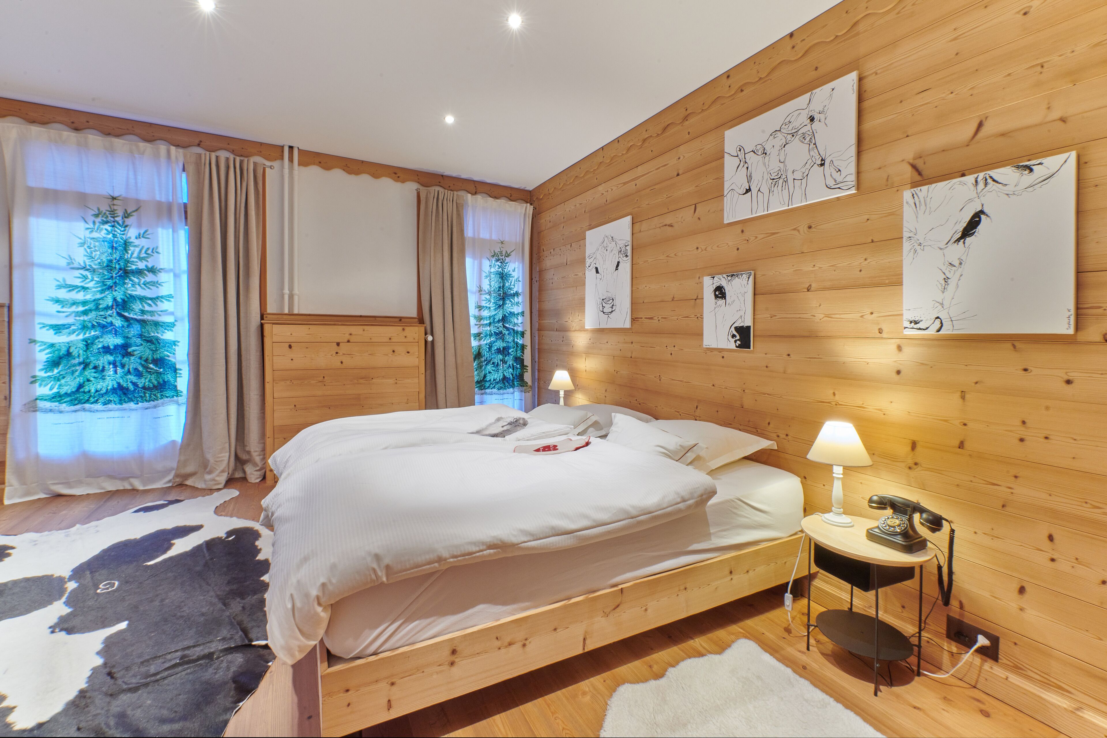 A wooden-paneled bedroom with a large bed, a nightstand with a lamp, and artwork on the walls.