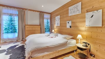 A wooden-paneled bedroom with a large bed, a nightstand with a lamp, and artwork on the walls.