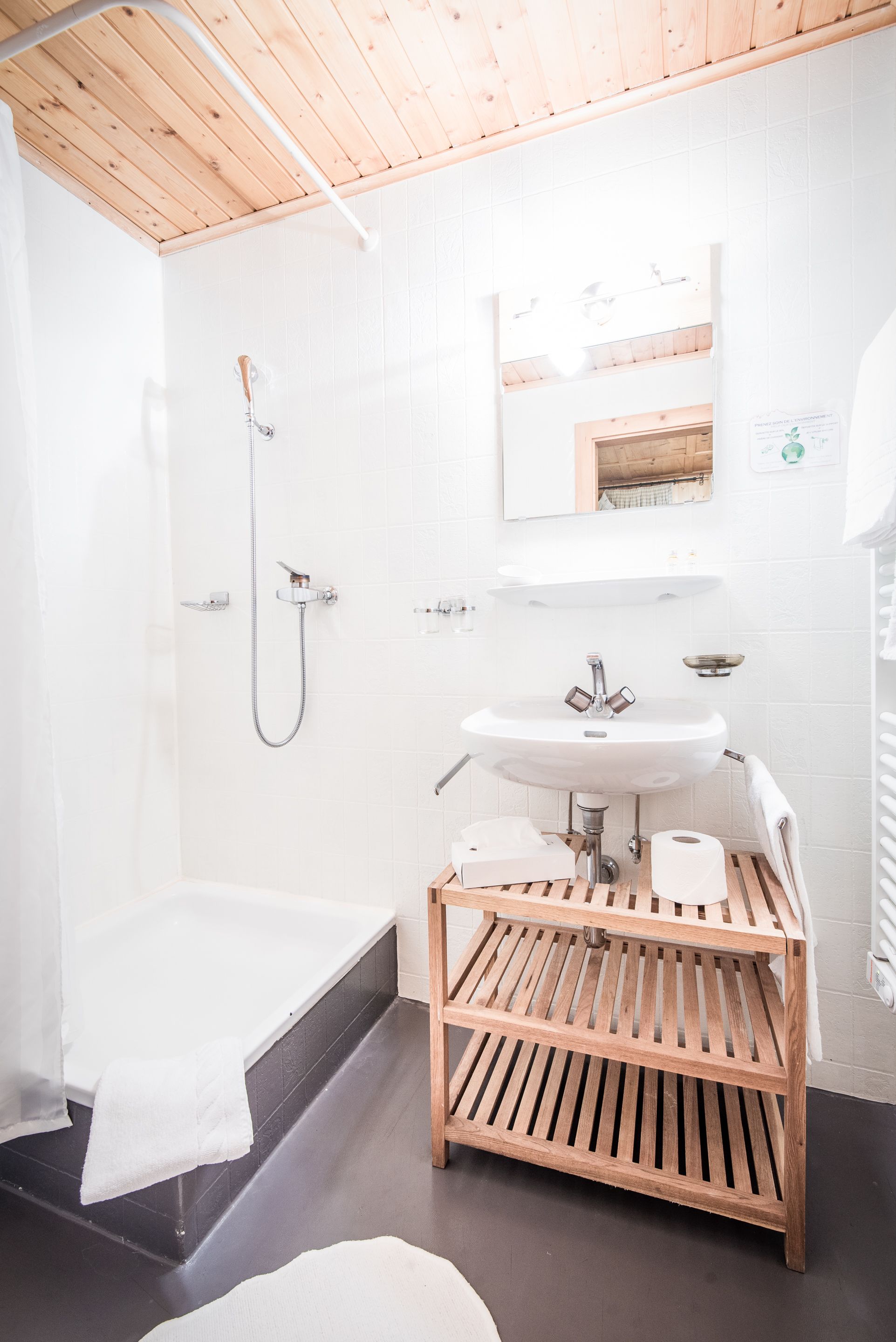 Un baño con techo de madera, azulejos blancos, una bañera, un lavamanos y un tocador de madera.