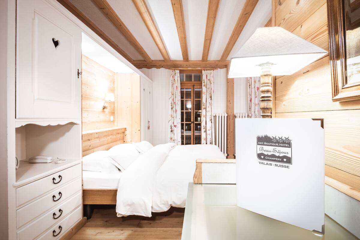 Ein Schlafzimmer mit Holzboden, einem Bett mit weißer Bettwäsche, einer Kommode mit Schubladen und einer Wandleuchte.