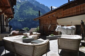 Een houten chalet met rieten meubilair en een koebeeld, met uitzicht op een bergachtig landschap.
