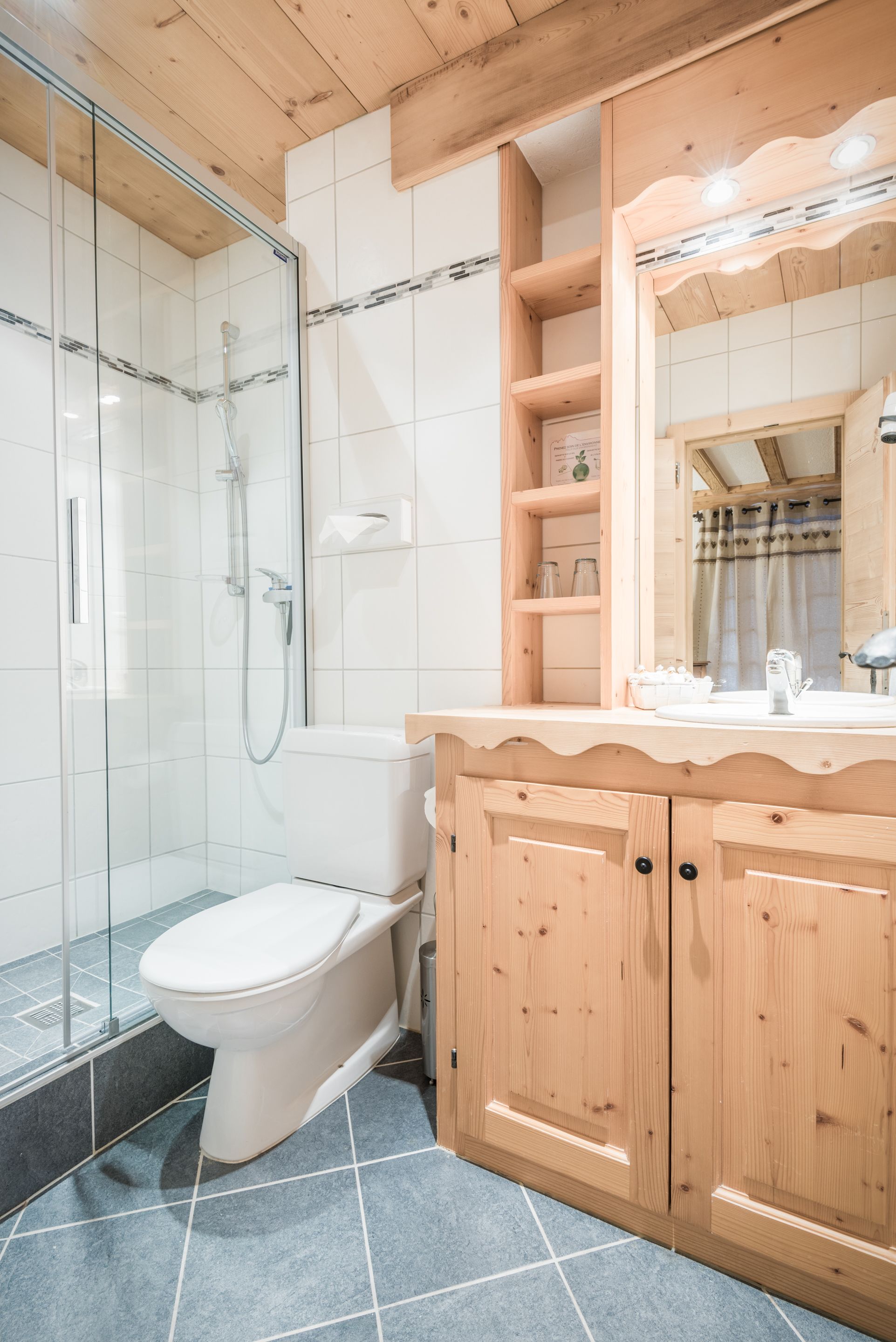 A modern bathroom with a glass-enclosed shower, a white toilet, and wooden cabinetry.