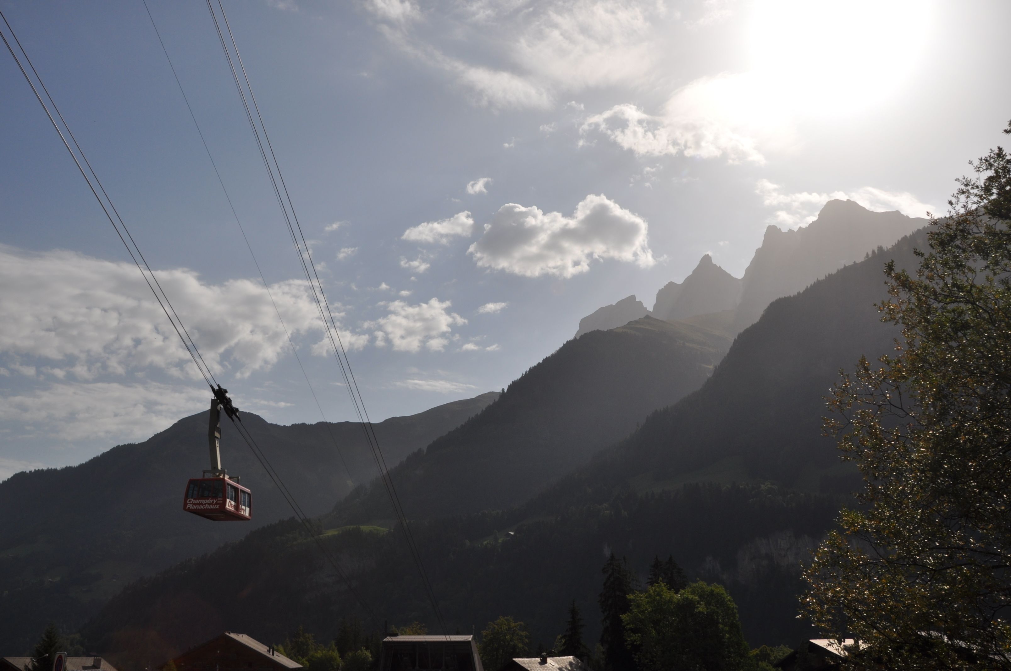 A cable car moving over a mountainous landscape with clear skies and a sunlit peak in the background.
