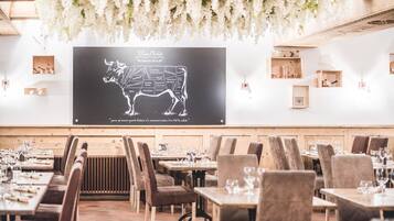 Ein Restaurant mit einer Tafel, die eine Bullenillustration und Text enthält, Holztische und -stühle sowie hängende weiße Blumen.