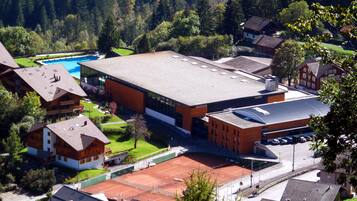 A large building with a flat roof, surrounded by residential houses and a tennis court.