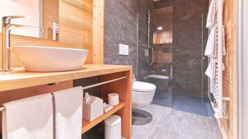 A modern bathroom with a wooden vanity, a large sink, a glass shower enclosure, and a toilet.