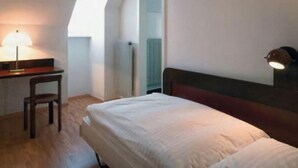 Une petite pièce bien éclairée, avec un lit, un bureau et une chaise, ainsi qu’un miroir.
