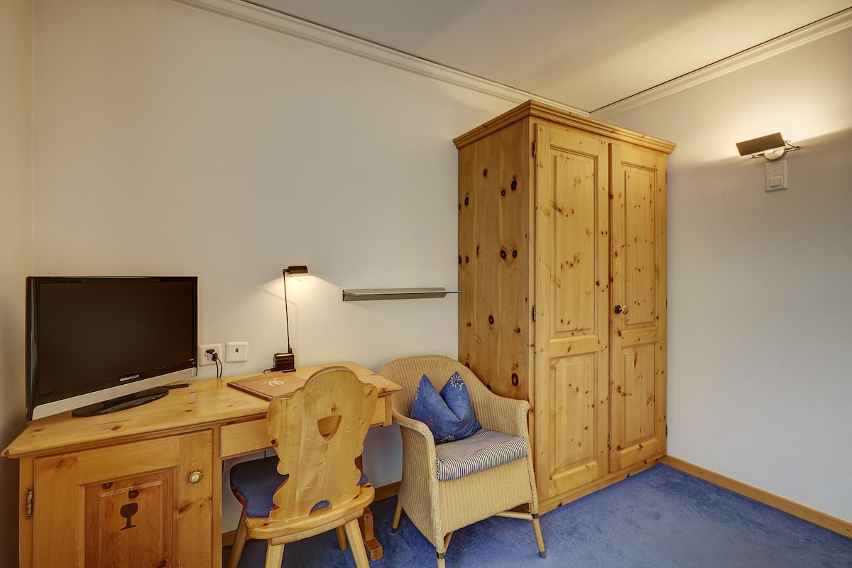 A room with a wooden desk, a television, a chair, a wardrobe, and a lamp.