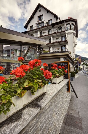 A multi-story building with balconies, a stone facade, and red flowers in front. - Hotel Meierhof (Davos)
