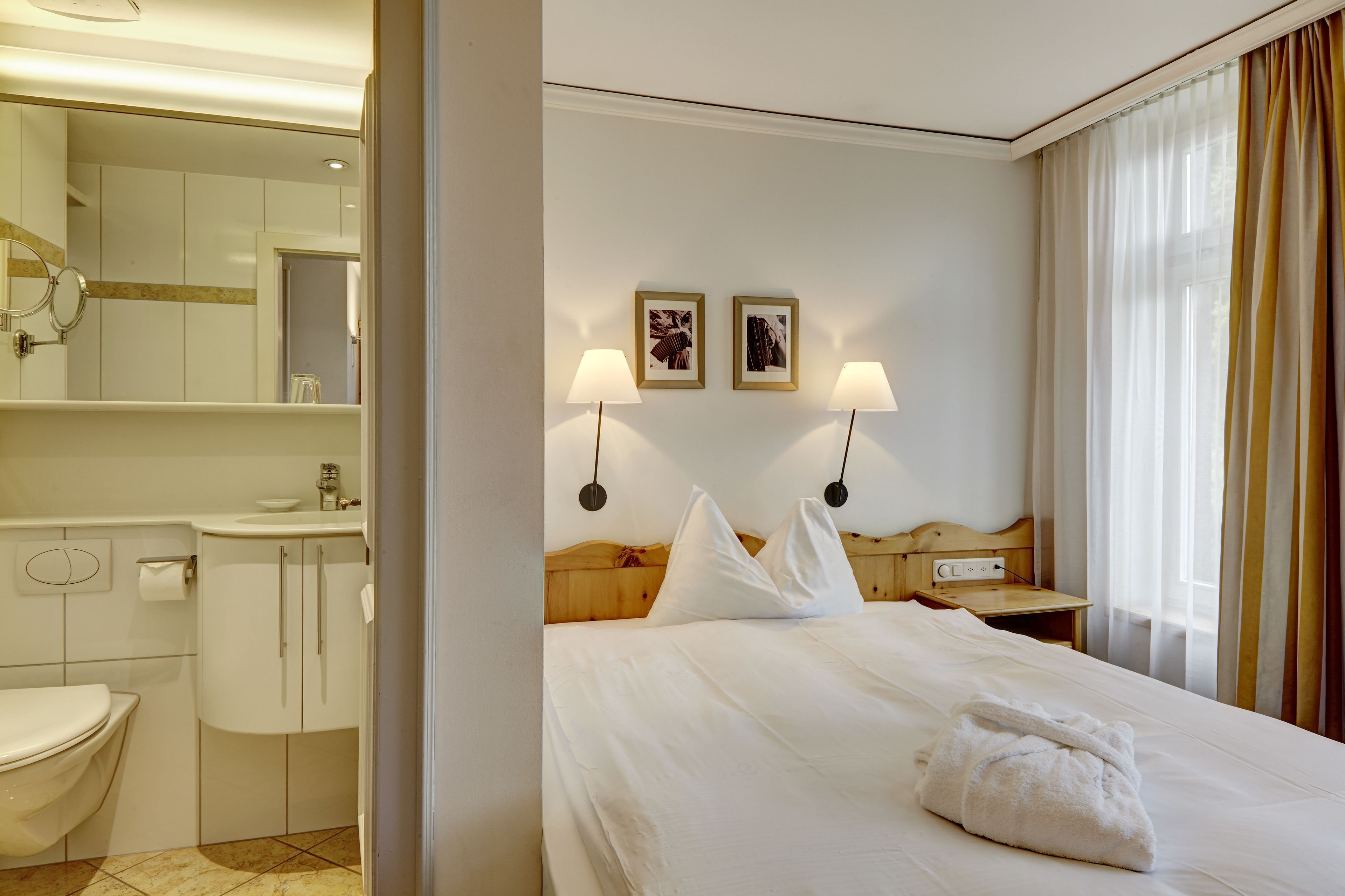 Een hotelkamer met een bed, nachtkastje, lamp, spiegel, wastafel en toilet.