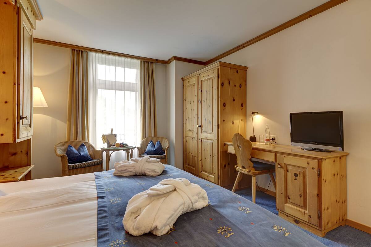 A hotel room with a bed, a desk with a television, a wardrobe, and a chair.