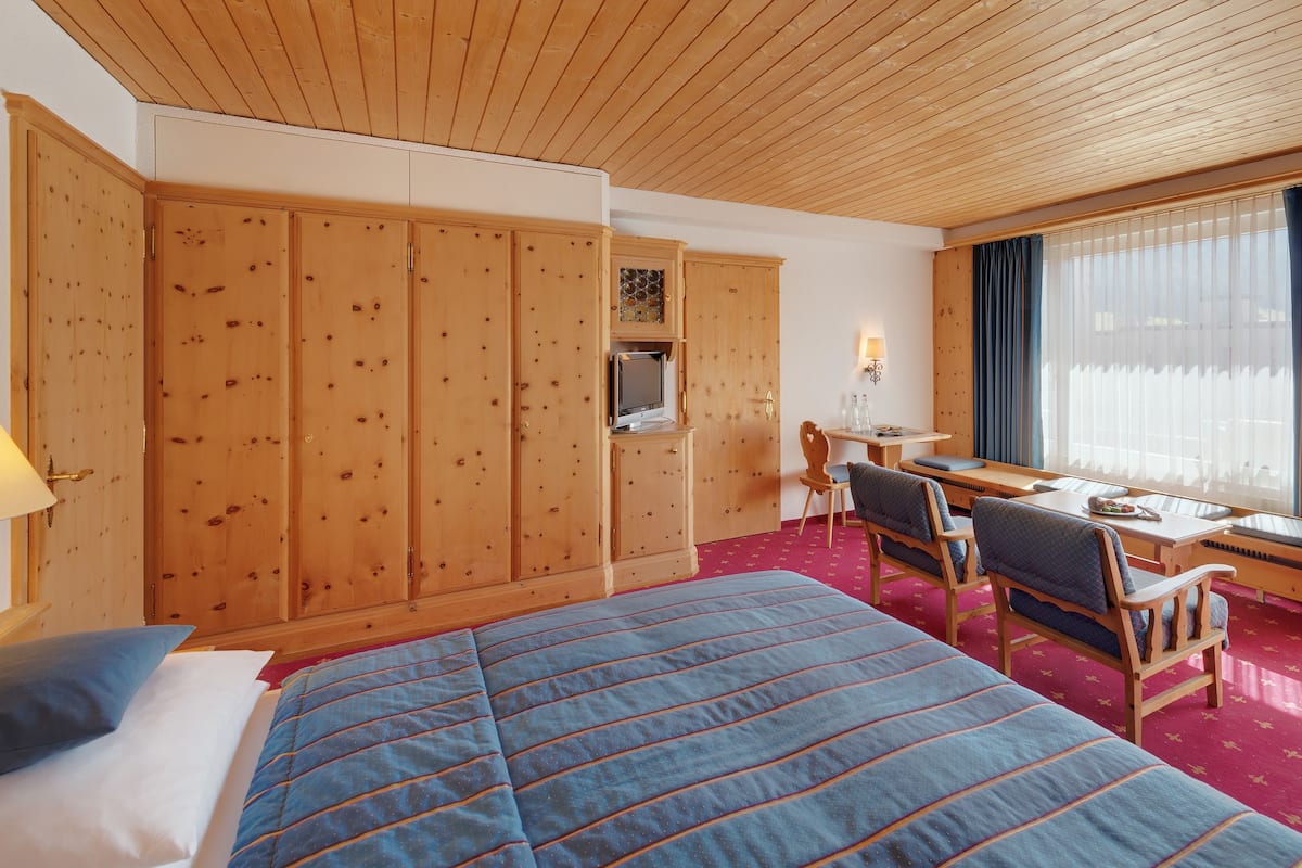 Ett hotellrum med en stor säng, en garderob i trä, ett skrivbord och en stol.