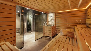 Een sauna met houten banken, een glazen deur naar een douchegedeelte en een stenen muur.