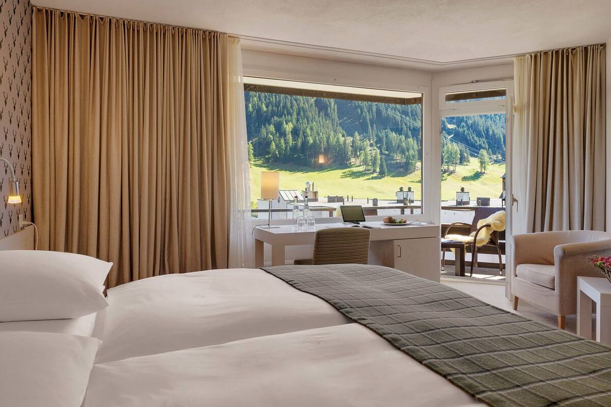 Ett hotellrum med en säng, ett skrivbord och utsikt över ett bergigt landskap.